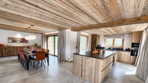 Una cocina amplia con vigas de madera, un comedor con una mesa larga y una isla grande con encimera negra.