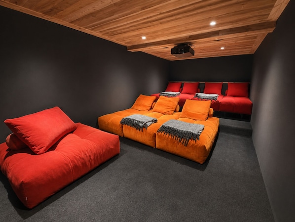 A room with a ceiling projector, a red sofa, and an orange couch with throw pillows.