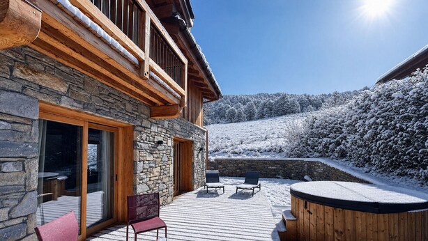 Un edificio de piedra con terraza de madera, asientos al aire libre y un jacuzzi.