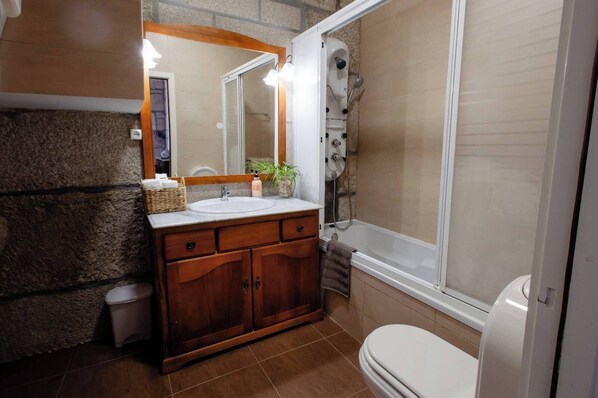 A bathroom with a stone wall, wooden vanity, white sink, and a bathtub with a showerhead.