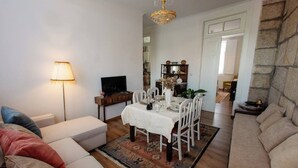 A living room with a sofa, a dining table set for four, a television, and a chandelier.
