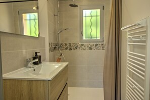 A bathroom with a sink, mirror, shower, and a window with a view.