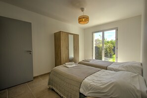 A bedroom with two beds, a wardrobe, and a window with a view of greenery.