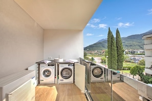 A balcony with three washing machines, a sink, and a view of a mountainous landscape. - Sole E Lago (Riva del Garda)