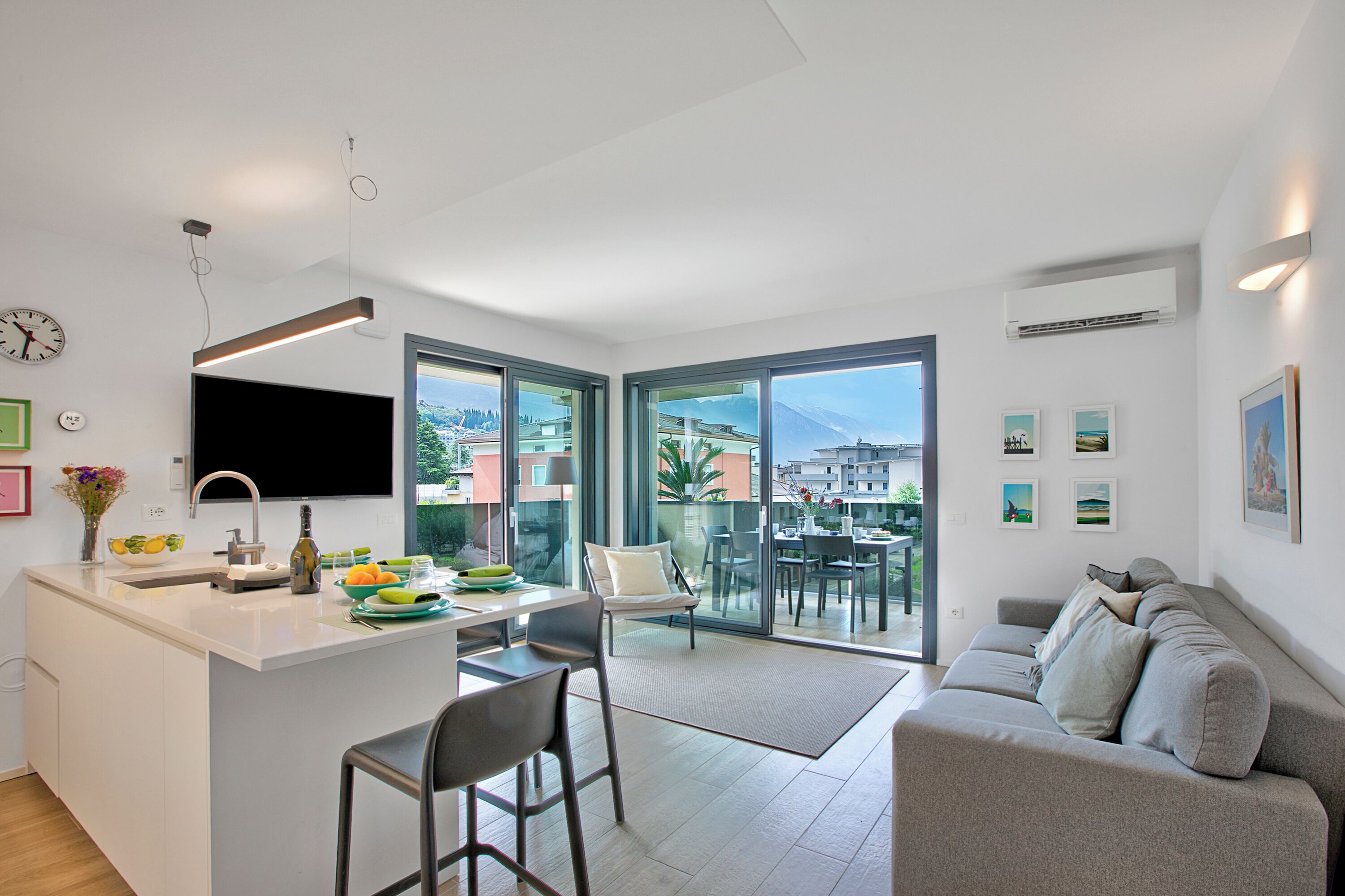 A modern kitchen with a central island, a dining area with a glass table, and a sofa in a living area with a city view.
