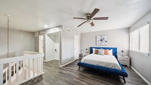 Ein Schlafzimmer mit einem blauen Bett, weißen Wänden, einem Deckenventilator und Holzboden.