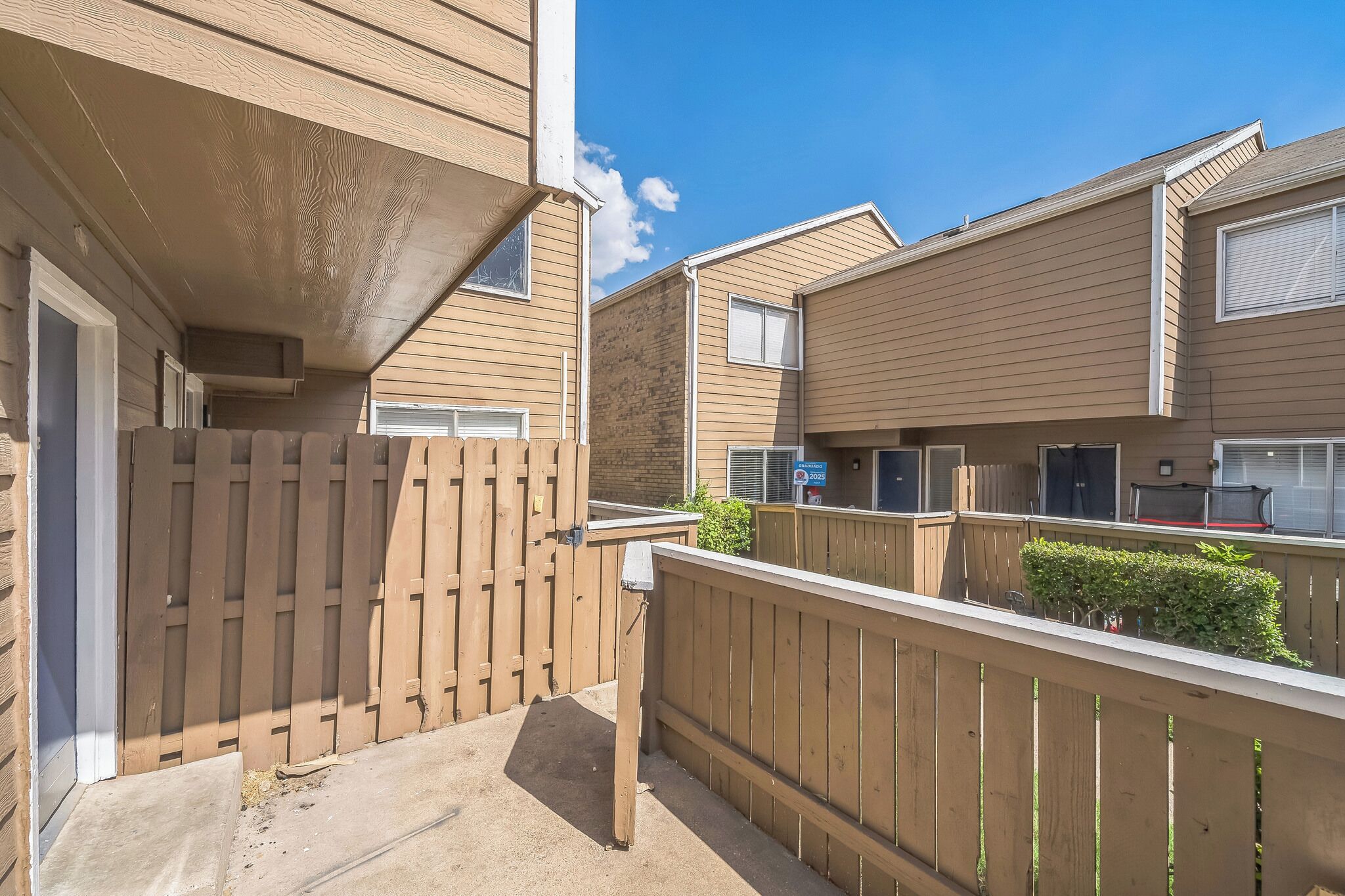 A residential building with a wooden deck, a small garden, and a clear blue sky.