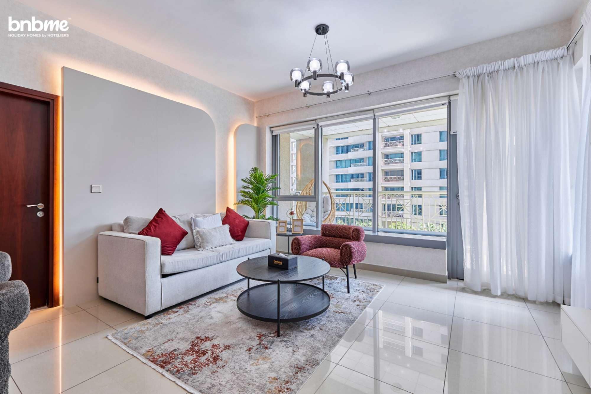 Ein modernes Wohnzimmer mit Sofa, Sessel und Couchtisch, großen Fenstern mit Blick auf die Stadt und einem Kronleuchter.