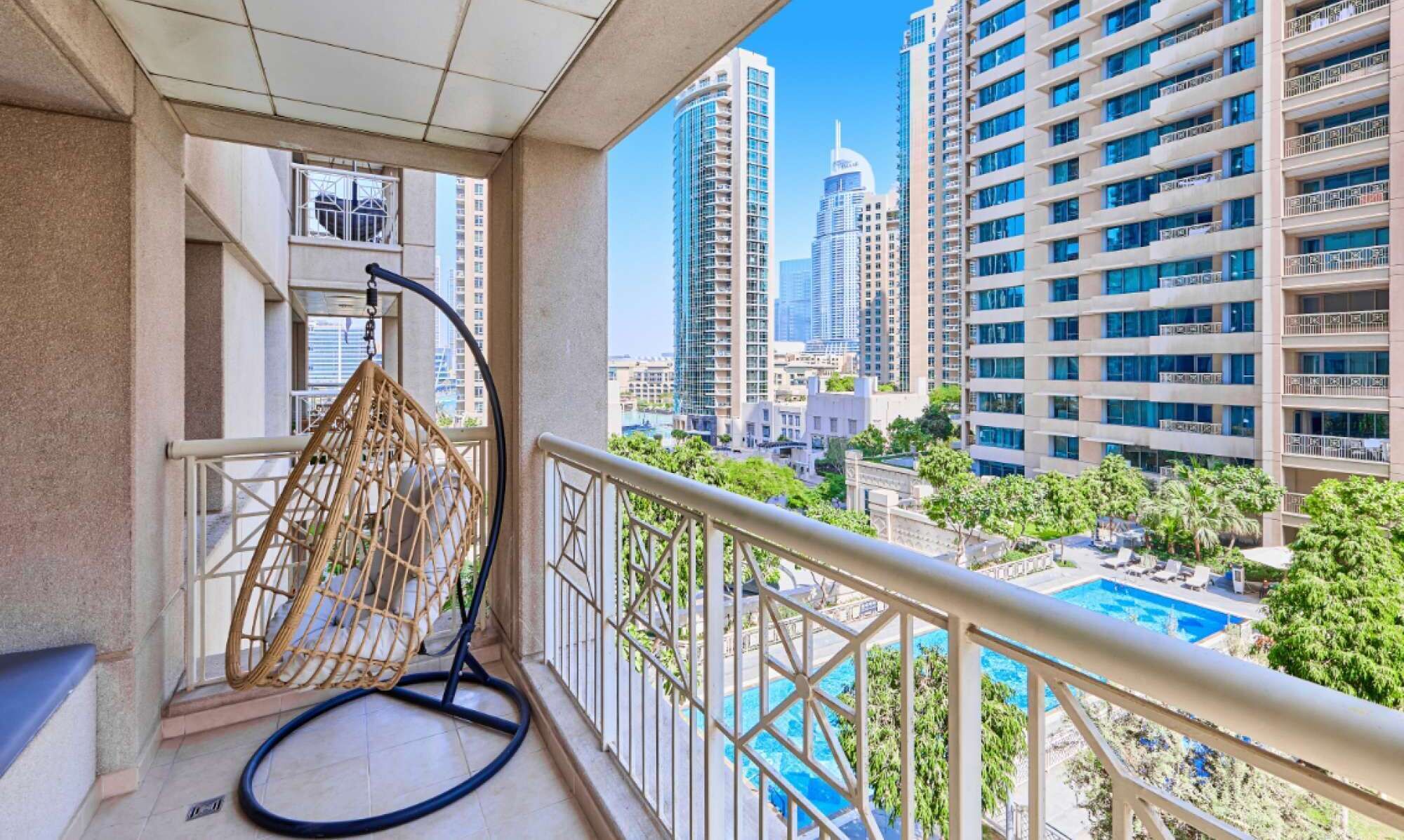 A balcony with a hanging chair, a pool, and high-rise buildings in the background.
