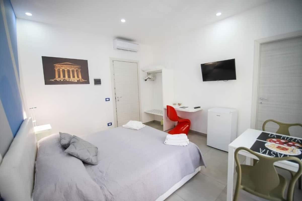 A hotel room with a bed, a desk, a chair, a TV, and a door.