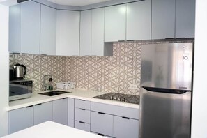 A modern kitchen with grey cabinets, a stainless steel refrigerator, a microwave, and a patterned backsplash.