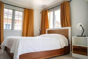 A bedroom with a bed, curtains, a bedside table, and a window.