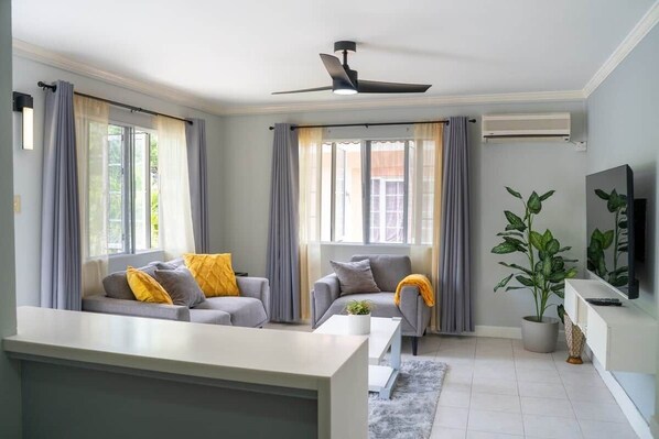 A modern living room with a sofa, a coffee table, a TV, and a ceiling fan.