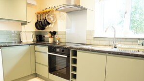 A modern kitchen with a built-in oven, a stainless steel range hood, and a window providing natural light. - Romantic Country Cottage with Private hot tub (Wiltshire)