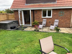 A brick house with a patio, a hot tub, and two lounge chairs. - Romantic Country Cottage with Private hot tub (Wiltshire)