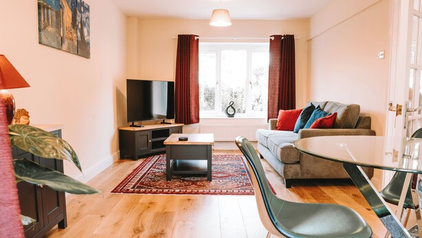 A modern living room with a sofa, TV, and dining area. - Romantic Country Cottage with Private hot tub (Wiltshire)