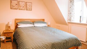 A bedroom with a bed, two bedside tables, a window with curtains, and three wall-mounted pictures. - Romantic Country Cottage with Private hot tub (Wiltshire)
