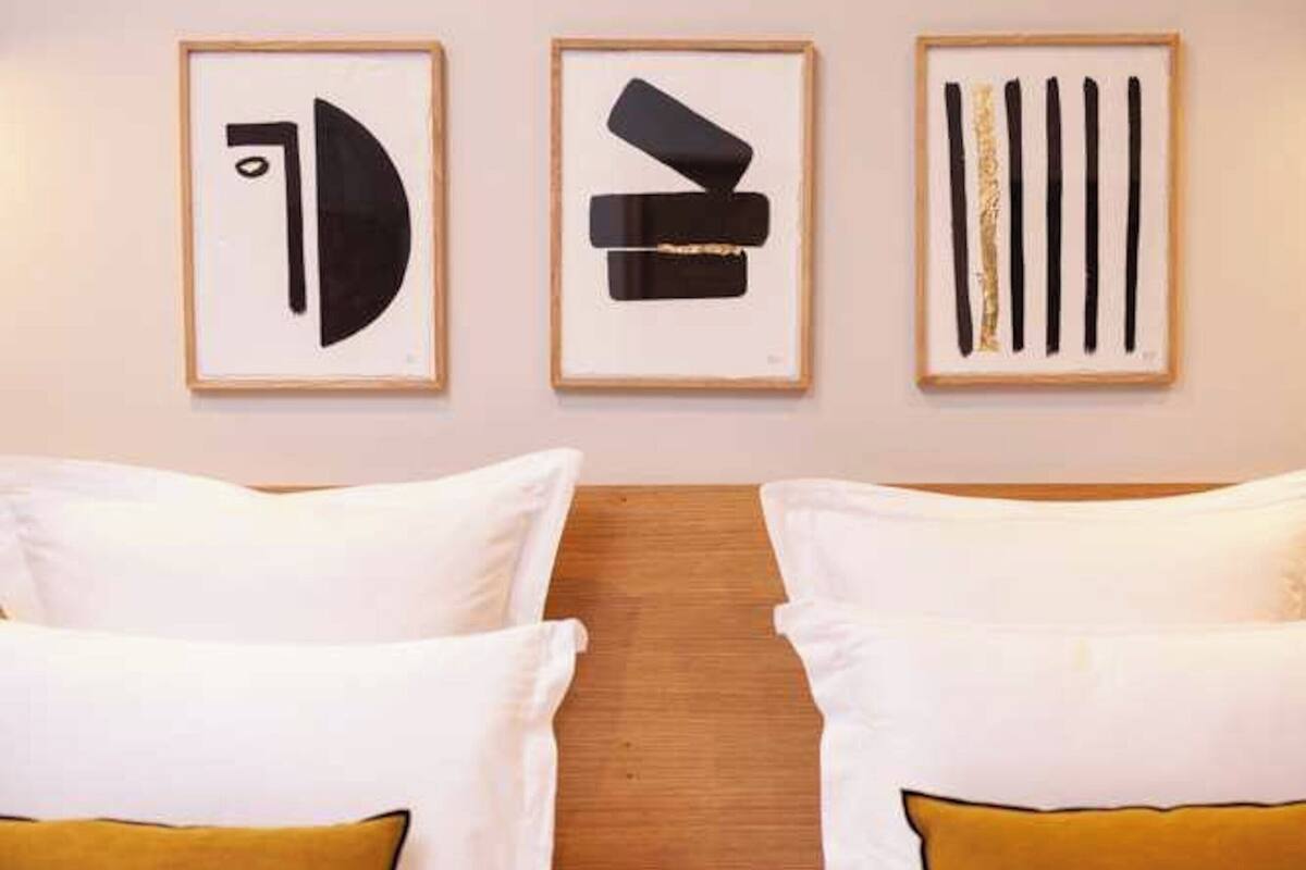 Une chambre d’hôtel avec un lit placé au centre, entre deux œuvres d’art abstraites encadrées qui ornent le mur.