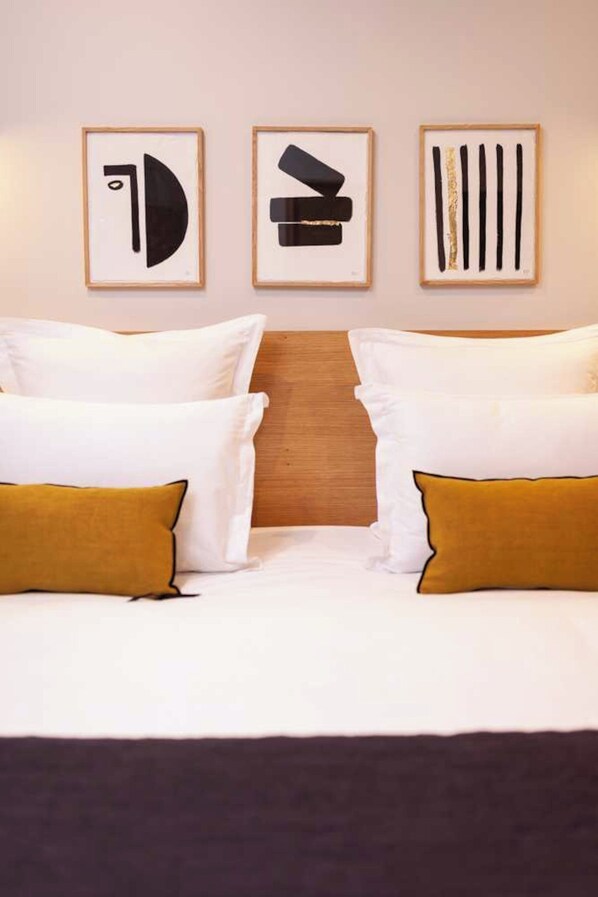 Ein Hotelzimmer mit einem Bett, das zwischen zwei gerahmten, abstrakten Kunstwerken an der Wand platziert ist.