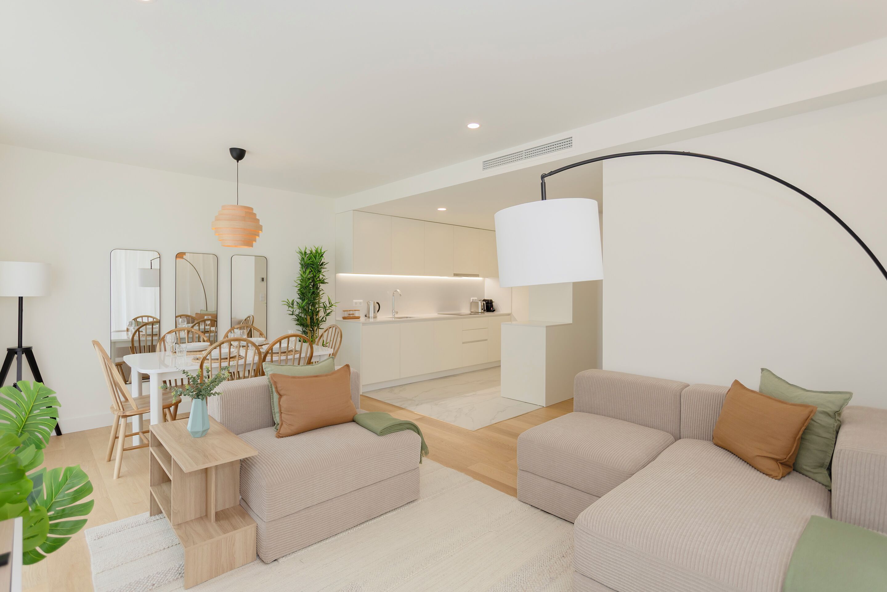 A modern living room with a sofa set, a dining table with chairs, and a kitchen area in the background.