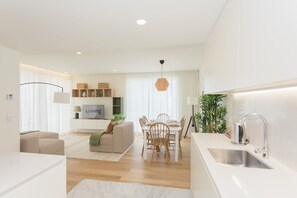 A modern kitchen with a dining area, a sofa, and a TV in the living room. - Liiiving - Factory Pearl Apartment (Matosinhos)