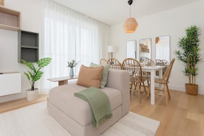 A modern living room with a sofa, dining table, chairs, and a potted plant. - Liiiving - Factory Pearl Apartment (Matosinhos)