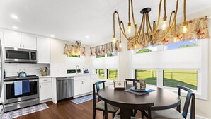 A modern kitchen with white cabinets, stainless steel appliances, and a dining area with a round table and chairs.