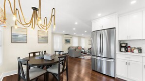 A modern kitchen with white cabinets, a stainless steel refrigerator, and a dining area with a wooden table and chairs.