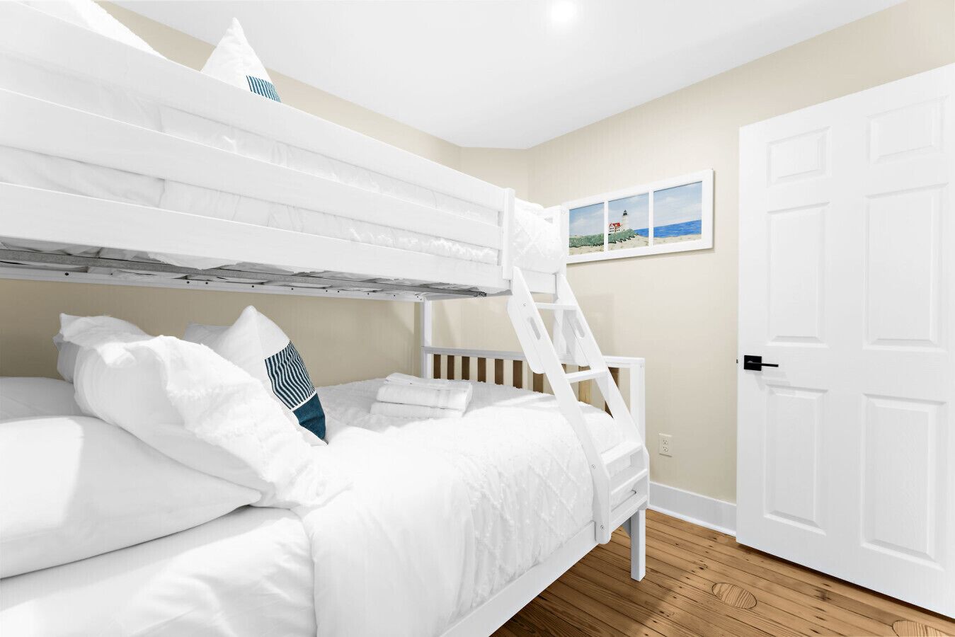Una cama litera con ropa de cama blanca y una escalera, una puerta blanca y un cuadro en la pared.