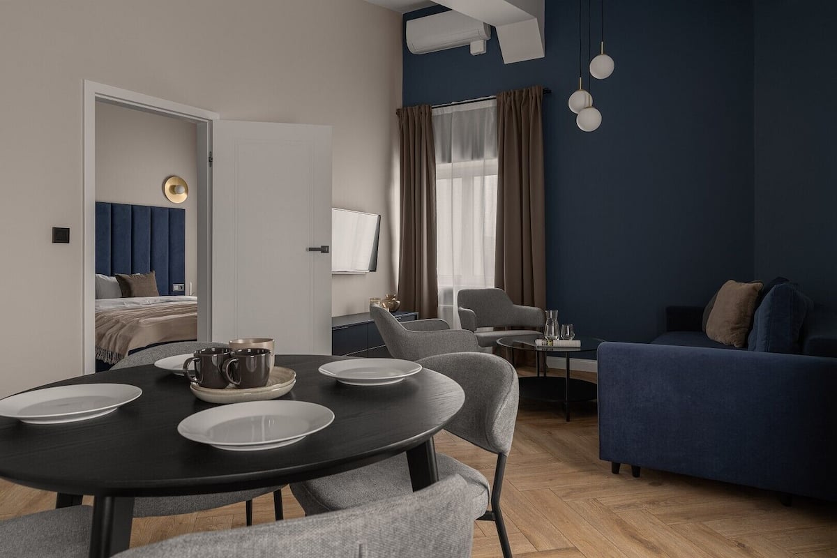 A modern living room with a dining area, a sofa, and a bed in the background.