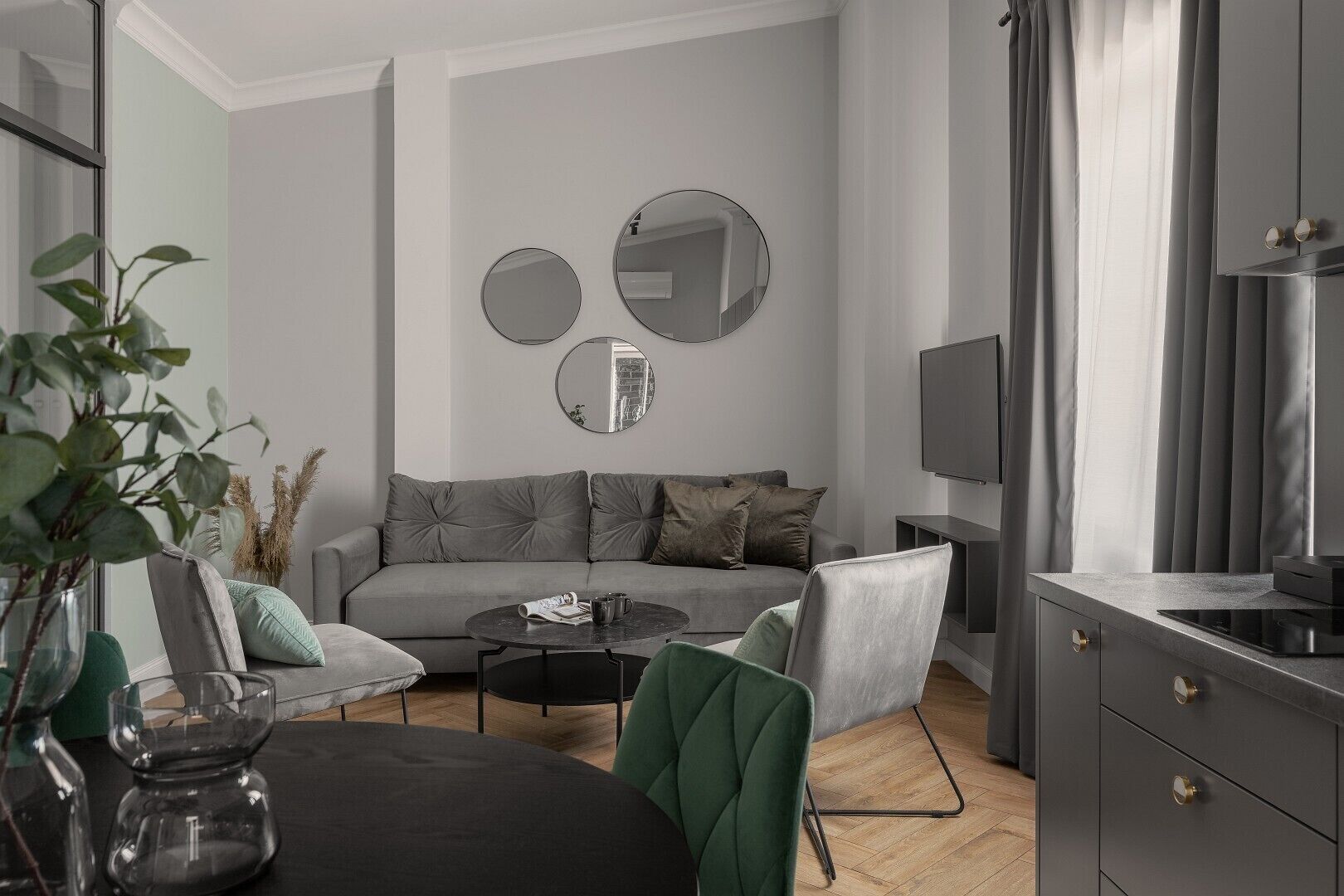 Een moderne woonkamer met een grijze bank, een bijzettafeltje en een televisie. Twee ronde spiegels hangen aan de muur en er staat een plant in de hoek.