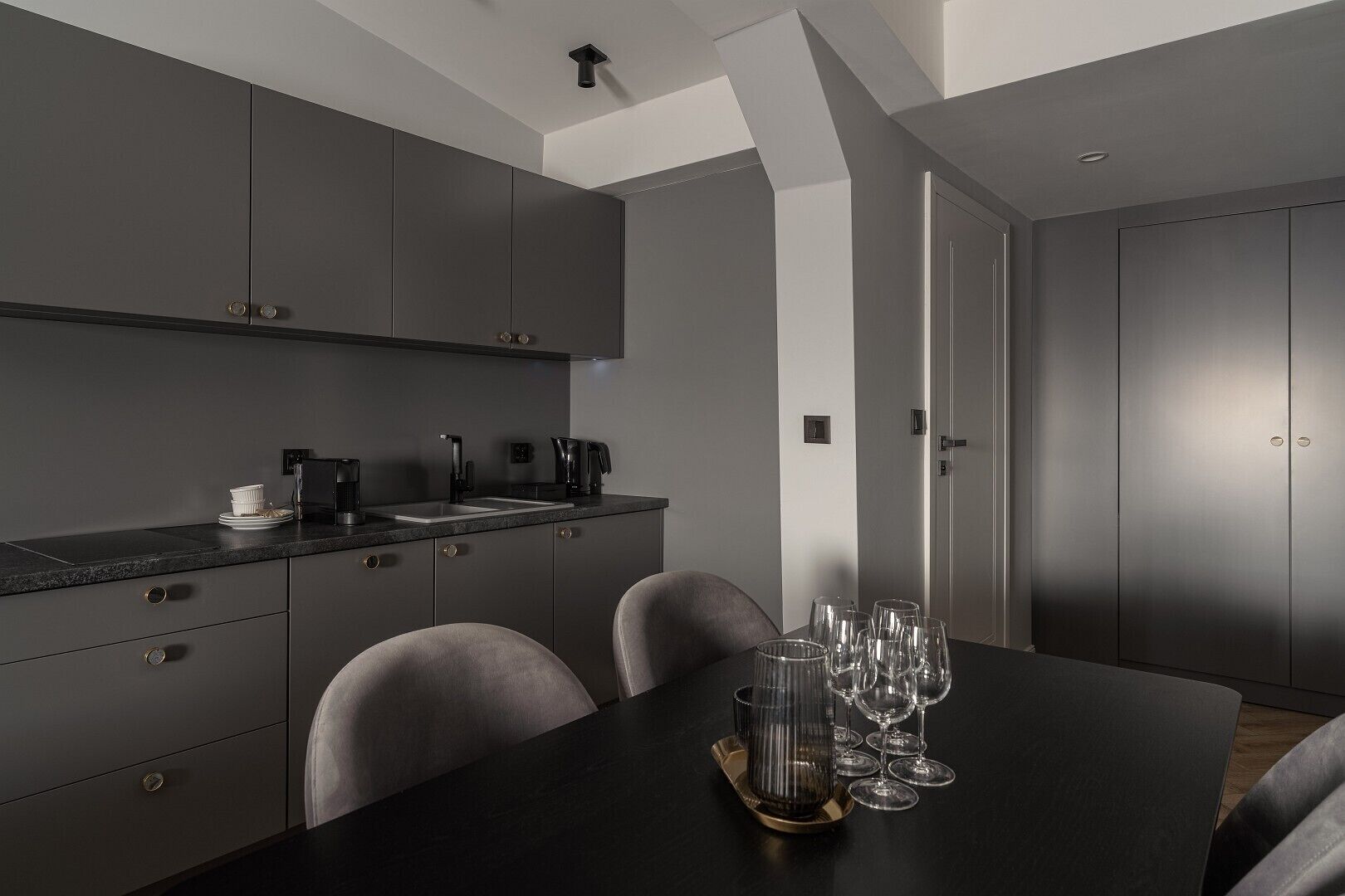 Una cucina moderna con mobili grigi, un piano di lavoro nero e un tavolo da pranzo apparecchiato con bicchieri da vino.