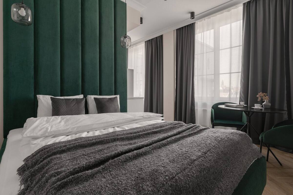 A modern hotel room with a large bed, dark green curtains, and a small table with a chair.