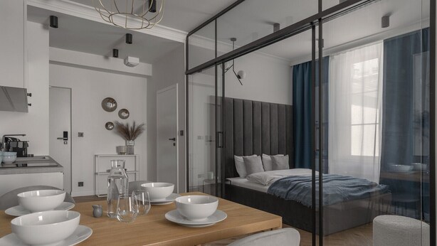 A modern hotel room with a dining area, a bed with a view, and a glass partition. - Apartio Rooms Katowice (Katowice)