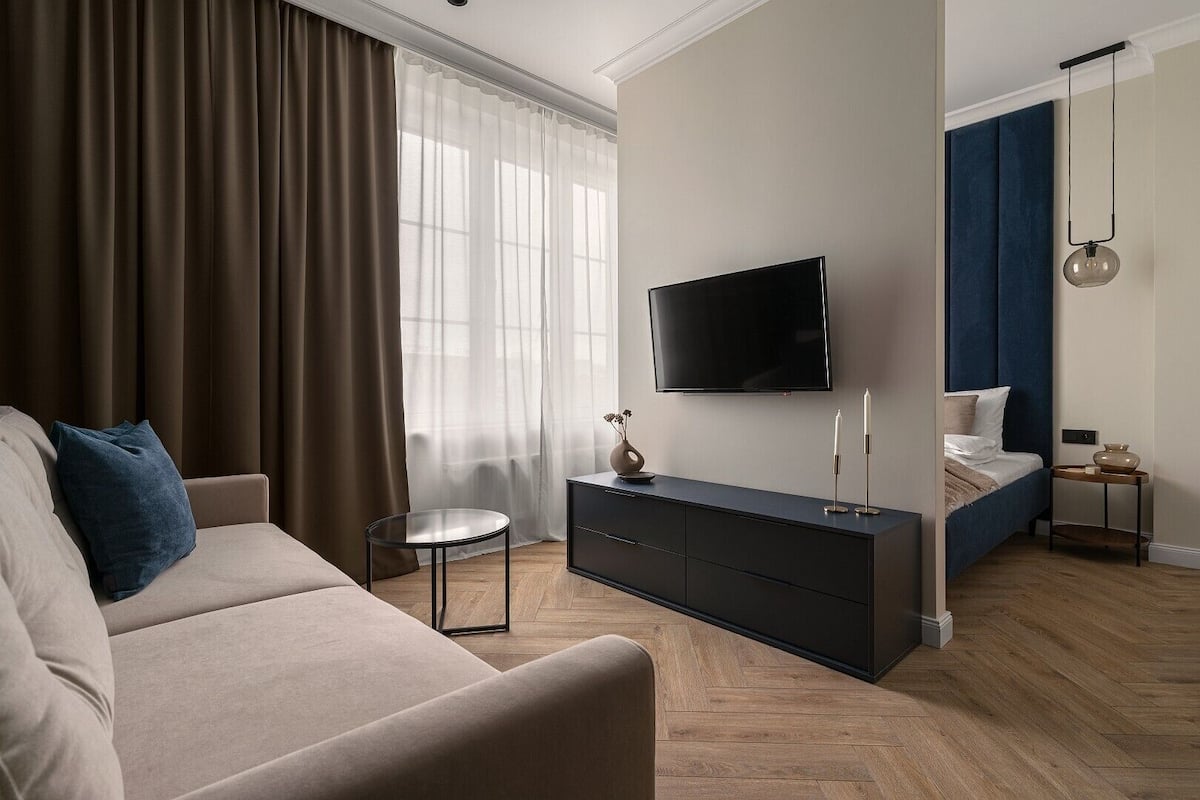 A modern hotel room with a flat-screen TV, a sofa, a bed, a bedside table, and a small side table with candles.