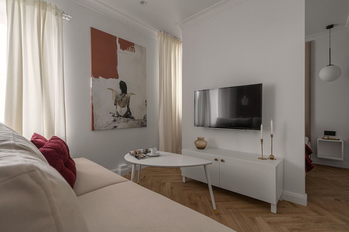 A modern living room with a white sofa, a round coffee table, a flat-screen TV mounted on the wall, and a minimalist decor style.