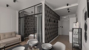 A modern dining area with a glass partition, a sofa, and a dining table set with plates and bowls. - Apartio Rooms Katowice (Katowice)