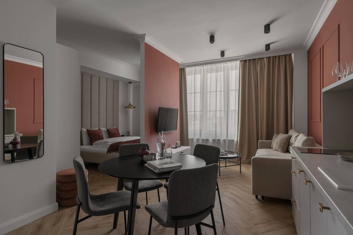 A modern hotel room with a dining area, a sofa, a TV, and a large window with curtains.