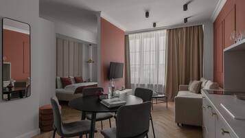 A modern hotel room with a dining area, a sofa, a TV, and a large window with curtains.