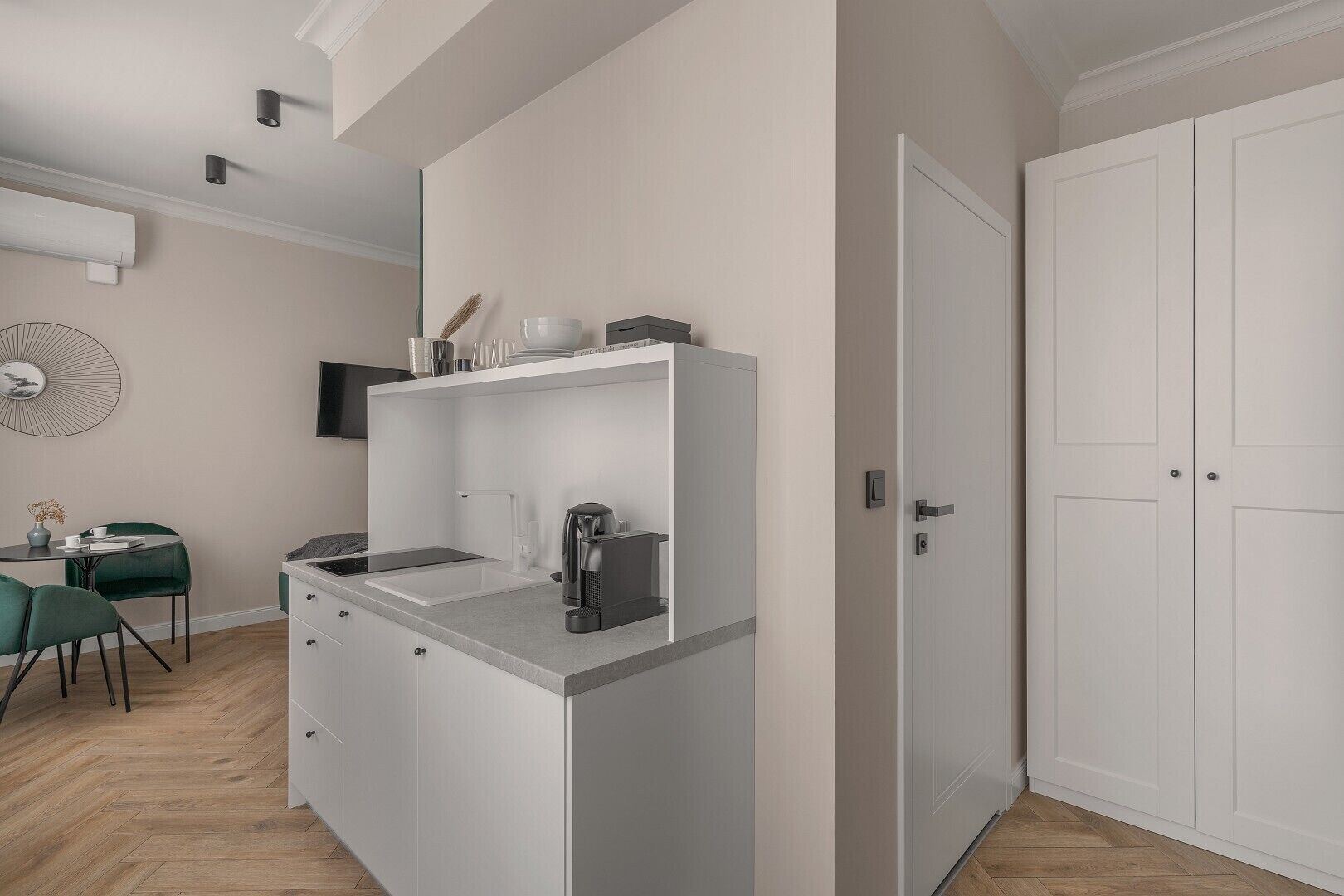 A compact kitchen with a sink, a coffee machine, and a small countertop. There is a dining area with a table and chairs.