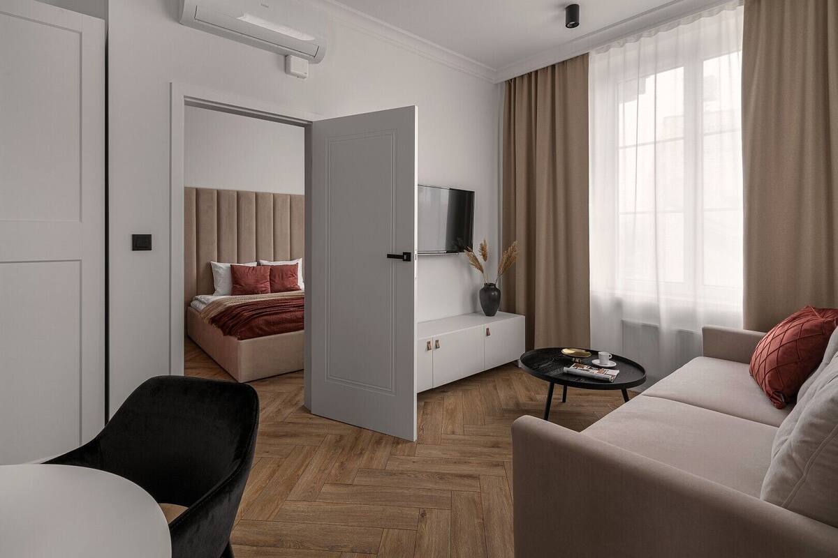 A modern hotel room with a bed, a sofa, a TV, and a small table.