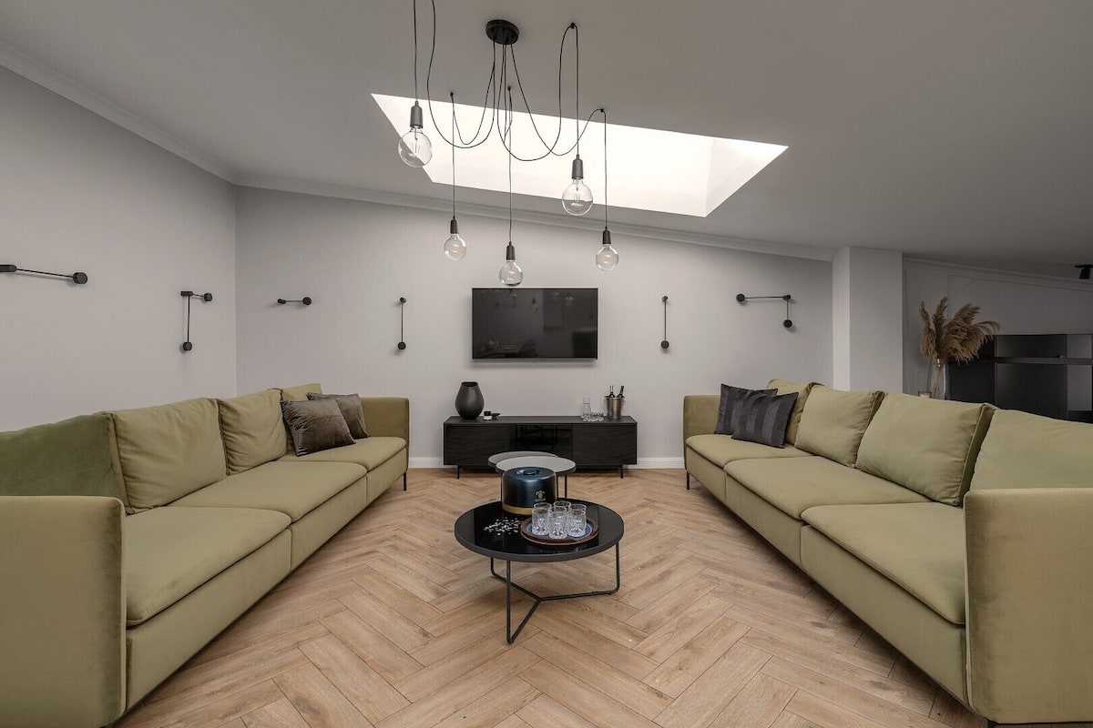 A modern living room with two sofas, a coffee table, a flat-screen TV, and pendant lights.