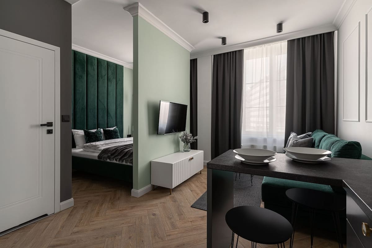 A modern hotel room with a bed, a TV, a dining area with a table and chairs, and a large window with curtains.