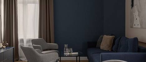 Una sala moderna con una pared azul oscuro de acento, una mesa redonda de comedor con sillas, un sofá y una lámpara colgante.