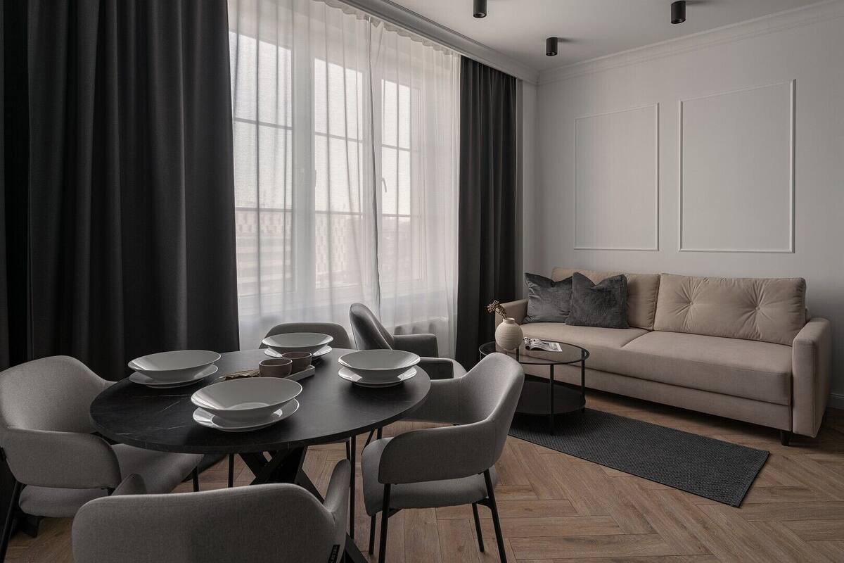A modern living room with a dining area, featuring a sofa, a coffee table, and a dining table set with plates and cups.