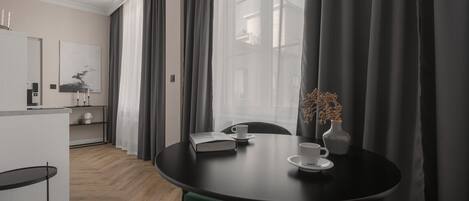 Ett modernt hotellrum med ett matbord, stolar, en vas med blommor och utsikt genom stora fönster.