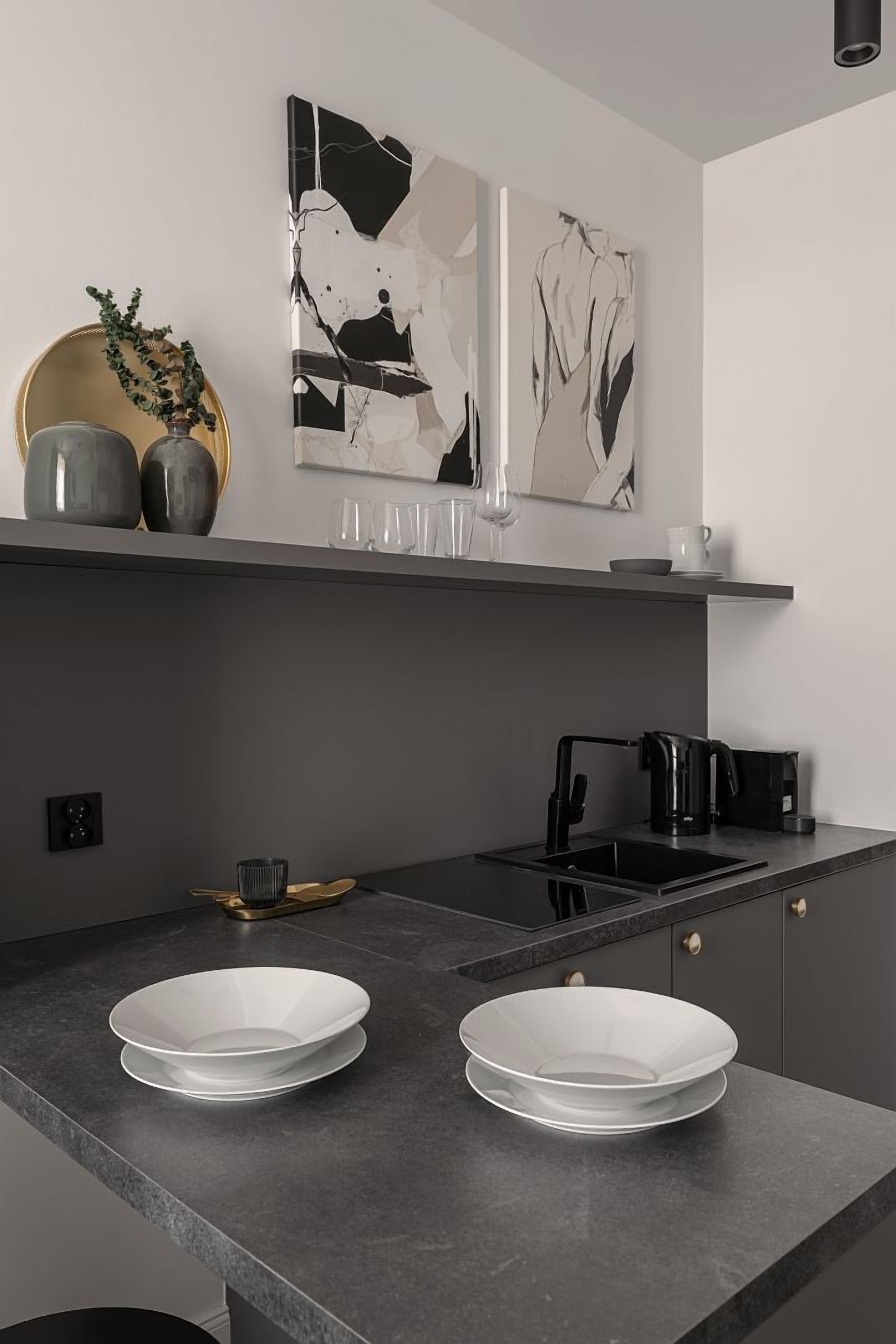Una cucina moderna con piani di lavoro scuri, due ciotole bianche, una macchina per il caffè e un'opera d'arte astratta appesa al muro.