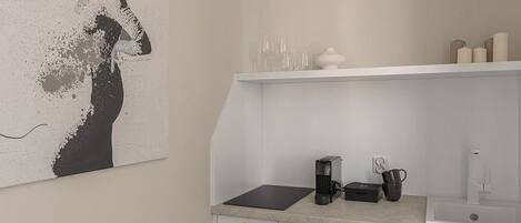 A modern kitchen with white cabinetry, a countertop with a coffee maker, and a wall-mounted light fixture.
