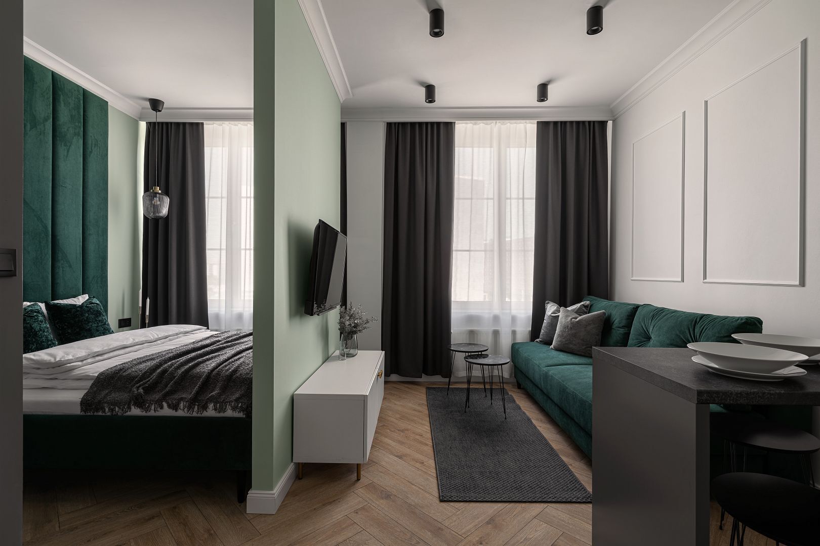 Una habitación moderna y bien iluminada con una cama, un sofá, una mesita y un televisor montado en la pared.