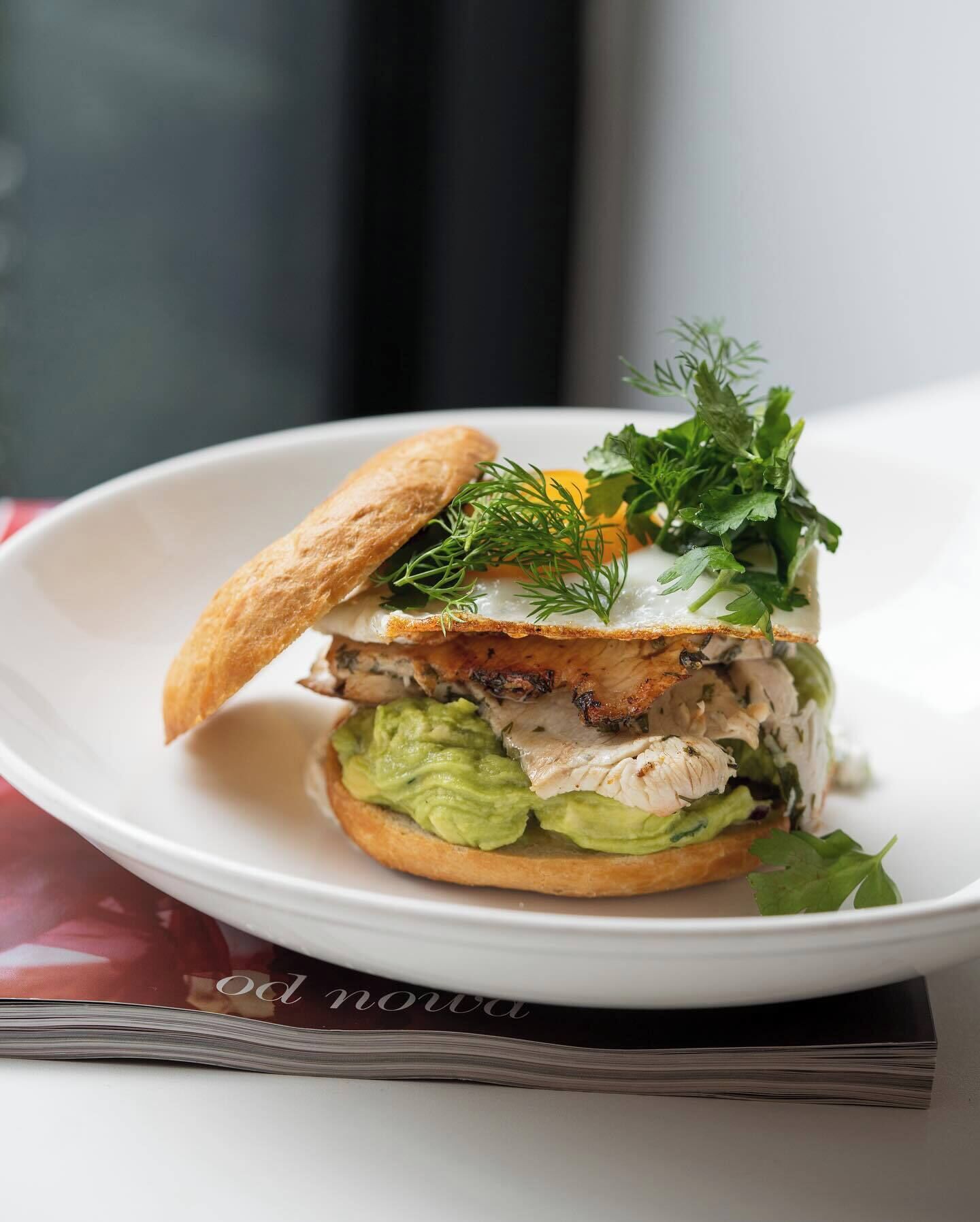 Un sándwich con aguacate, pollo y un huevo escalfado sobre un plato blanco.